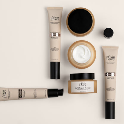 A flat-lay arrangement of Skin Diary skincare products on a warm off-white background, including two Age defence tubes, a jar of night repair therapy cream, an open jar showing white cream.