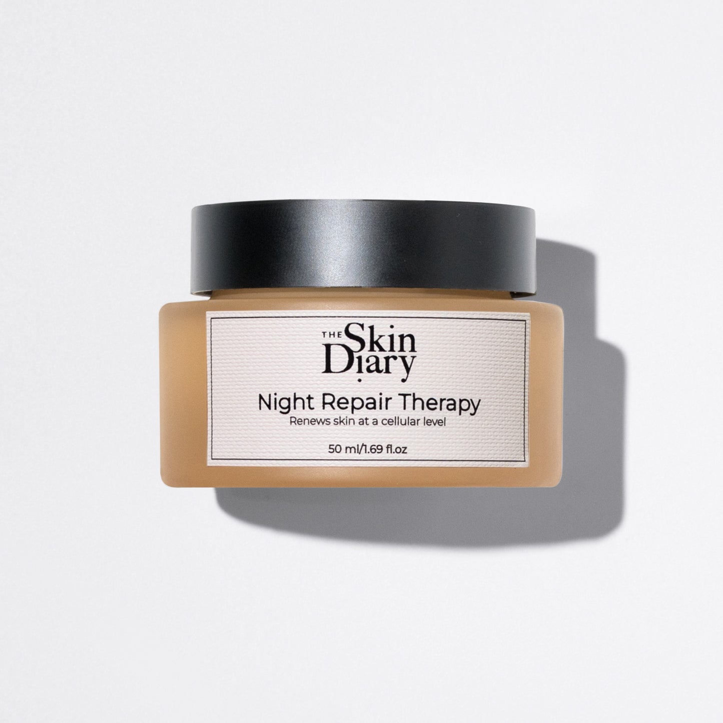 A jar of The Skin Diary Night Repair Therapy cream with a black lid and a amber glass container, shown on a white background with a soft shadow.